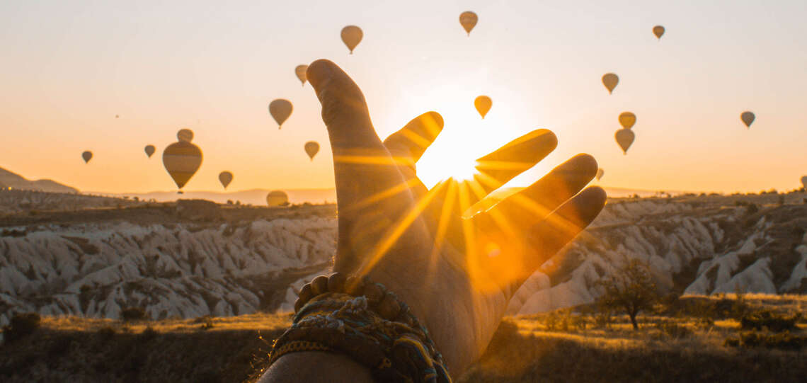 Hand im Sonnenaufgang und Heißluftballons im Hintergrund